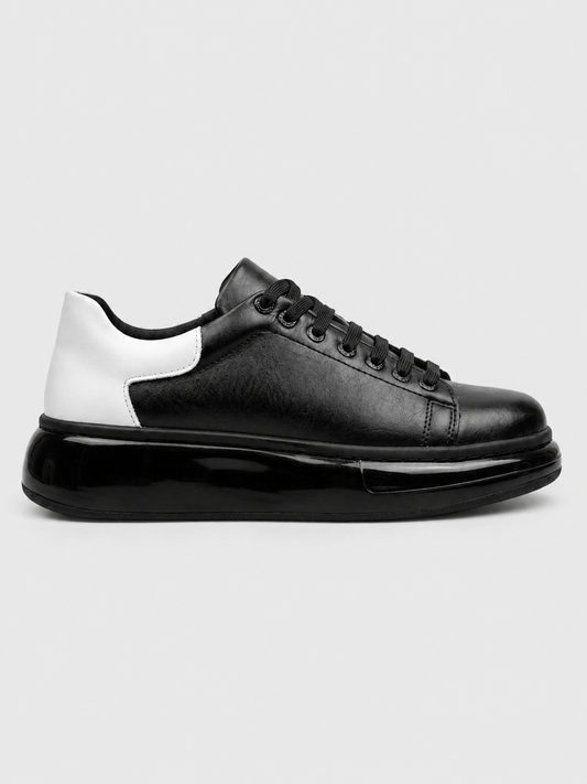 A black leather low-top sneaker with a chunky black platform sole and a contrasting white heel panel, shown in a side profile on a light gray background.
