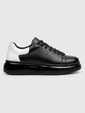 A black leather low-top sneaker with a chunky black platform sole and a contrasting white heel panel, shown in a side profile on a light gray background.